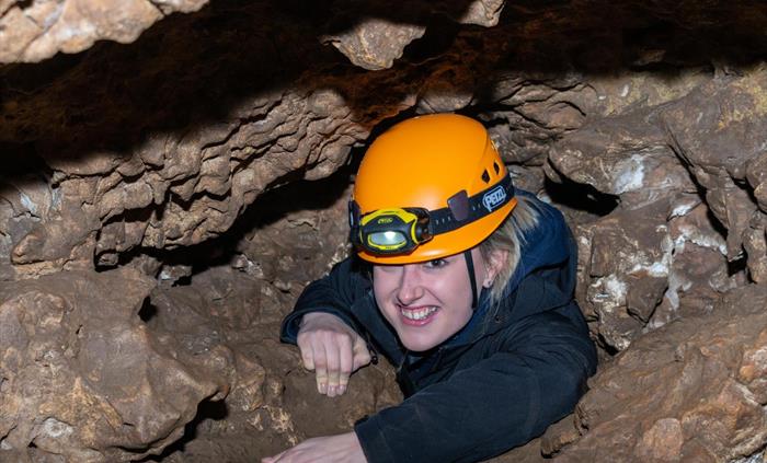 Lady wearing helmet crawling up through cave